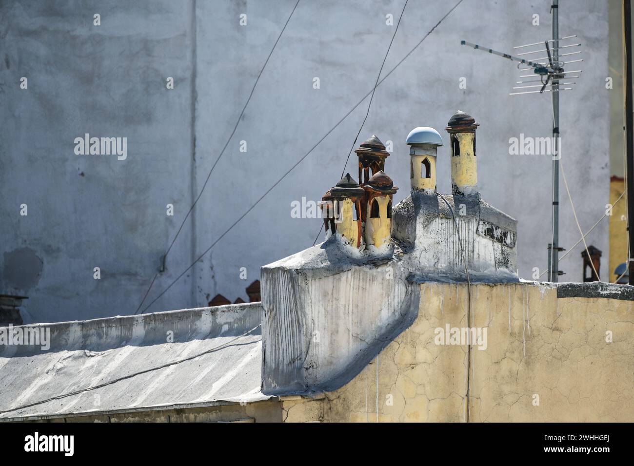 Kleine mediterrane Schornsteintöpfe mit verschiedenen Kappen, die wie ein kleines Dorf auf dem Dach eines traditionellen Apartments aussehen Stockfoto