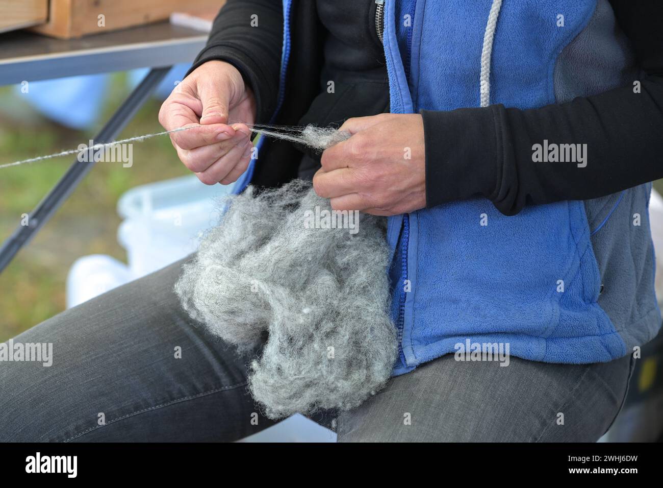 Hände einer Frau, die auf einem Handwerksmarkt rohe graue Wolle in Garn spinnt, ausgewählter Fokus Stockfoto