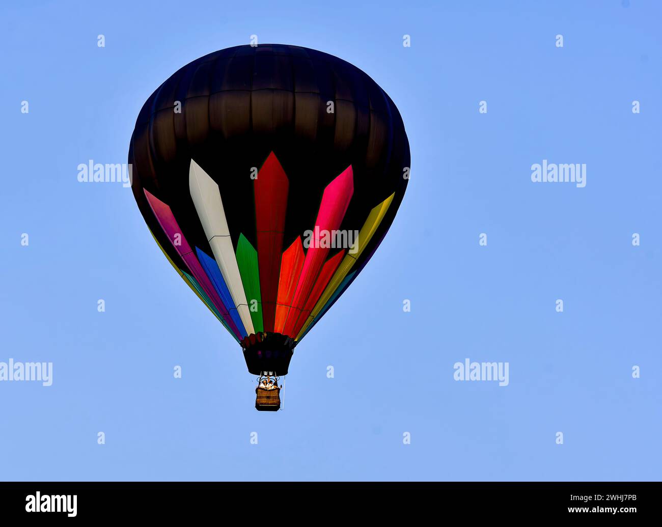 Blick auf einen Heißluftballon, Schwarz mit farbigen Streifen, die in einem All Blue Sky fliegen Stockfoto