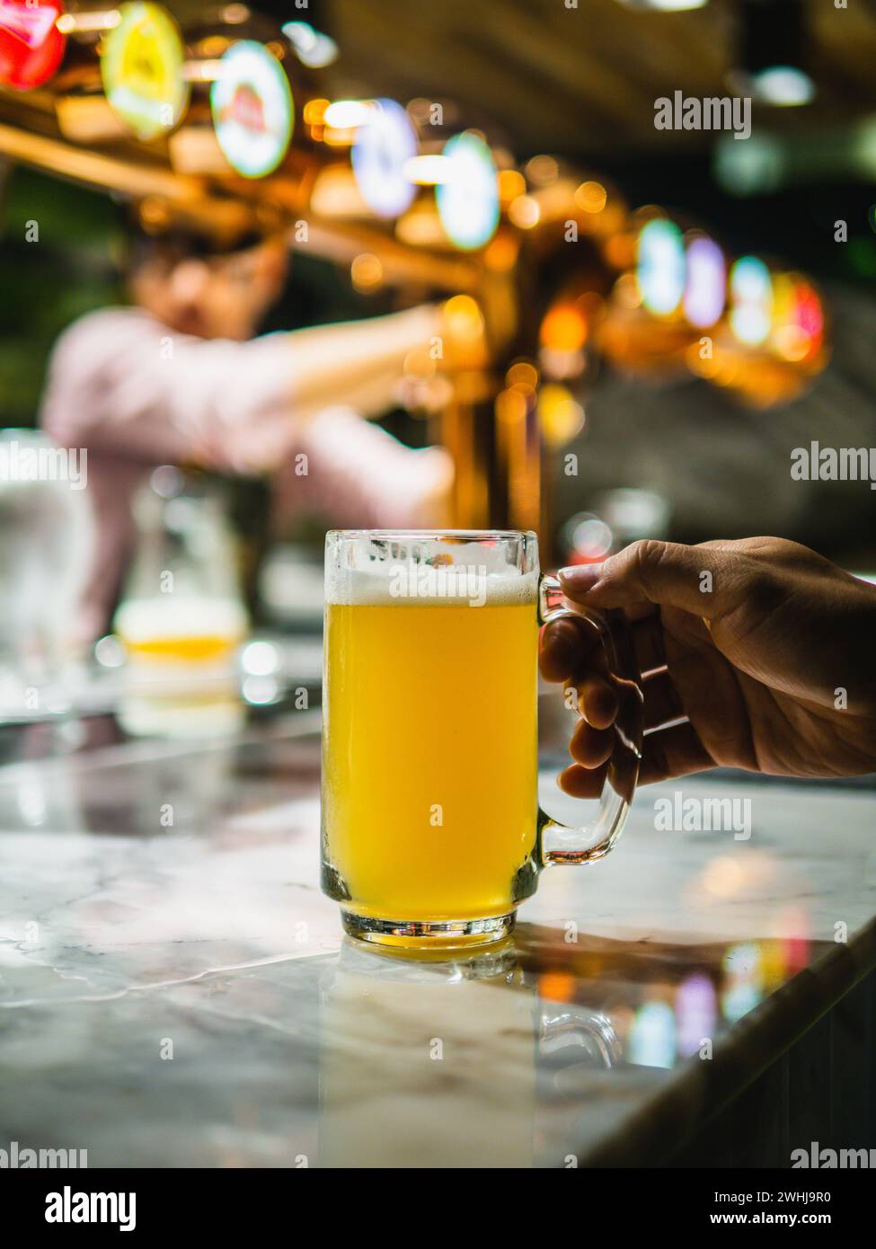 Frisch gezapftes Bier. Hand hält ein frisch gezapftes Glas Bier. Craft-Bier in ein Glas gegossen. Der Barkeeper gießt ein großes Lagerbier im Zapfhahn ein Stockfoto