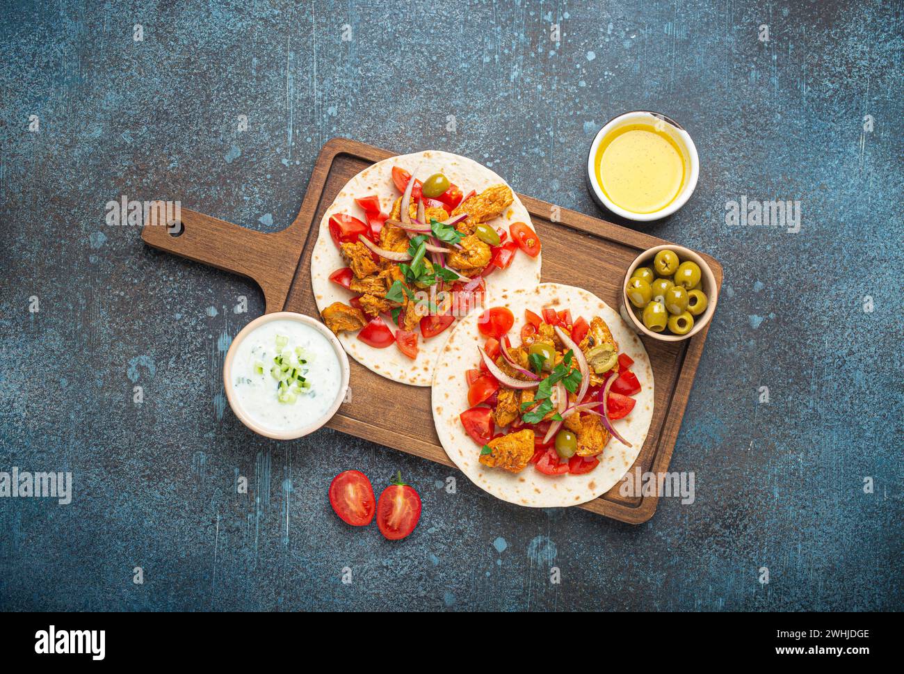 Traditionelles griechisches Gericht Gyros: Pita-Brot mit Gemüse, Fleisch, Kräutern, Oliven auf rustikalem Holzschneidebrett mit Tzatzi Stockfoto