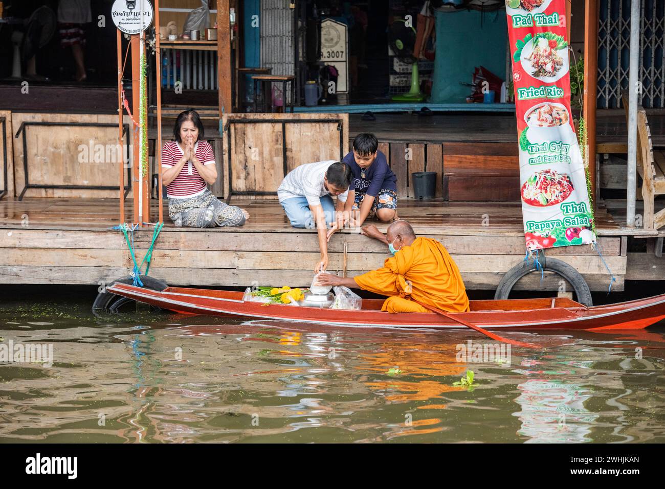 Ein buddhistischer Mönch auf seiner Morgenalmose, der eine Tour auf einem Holzboot am Damnoen Saduak und auf dem schwimmenden Markt in der Provinz Ratchaburi in Thailand, Th, macht Stockfoto