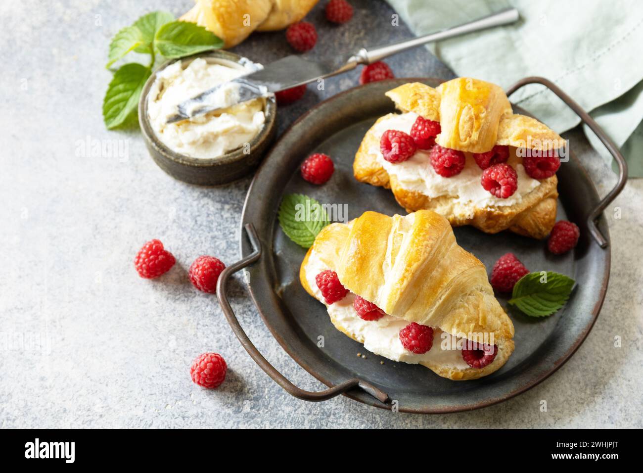 Gesundes Essen Dessert Konzept, französisches Gebäck. Leckere frisch gebackene Croissants mit Frischkäse und Himbeere auf einem Steinhintergrund Stockfoto