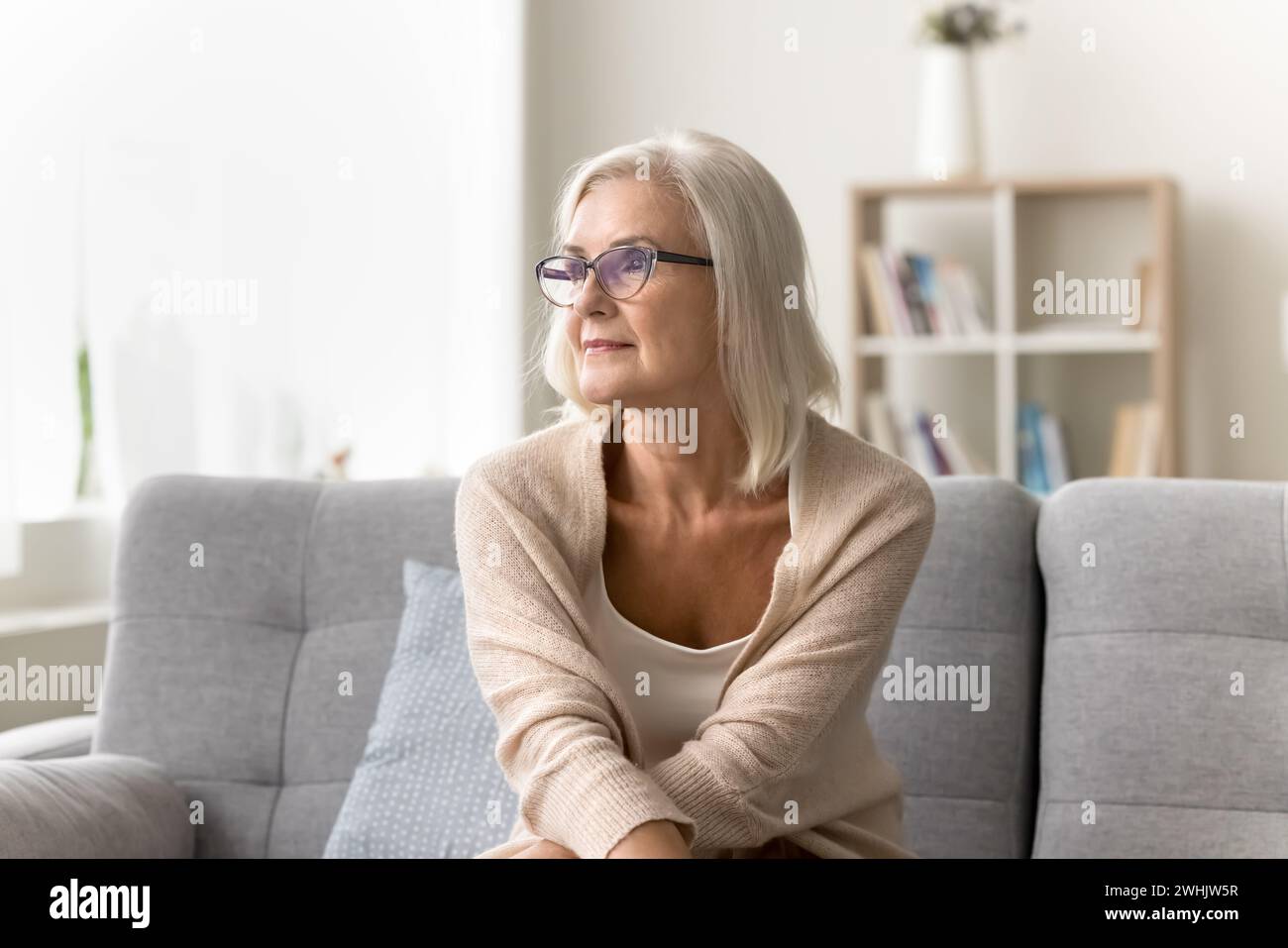 Eine durchdachte, hübsche, blonde Seniorin mit einer stilvollen Brille Stockfoto
