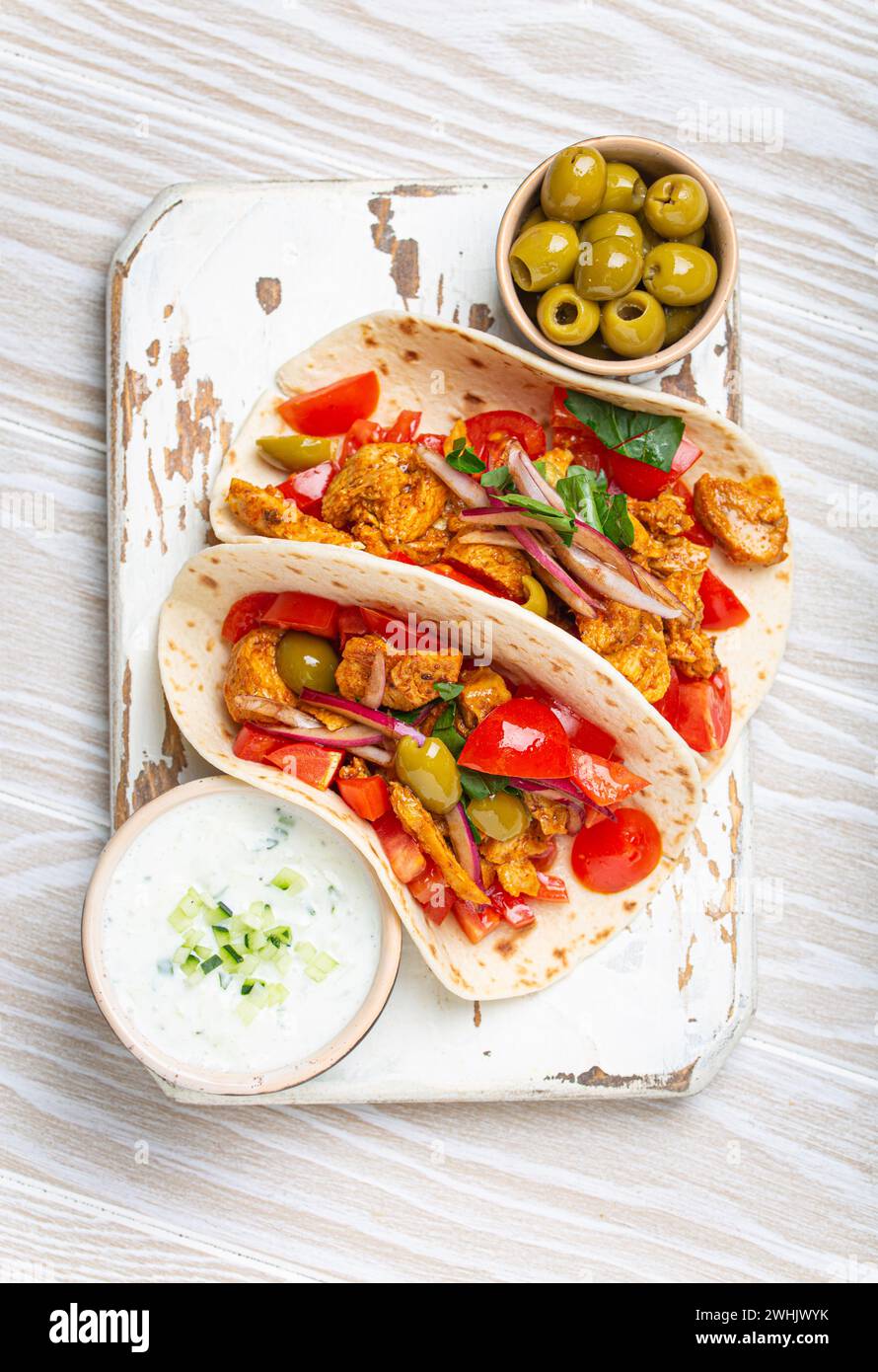 Traditionelles griechisches Gericht Gyros: Pita Brotwickel mit Gemüse, Fleisch, Kräutern, Oliven auf rustikalem Holzschneidebrett mit Tzatziki Stockfoto