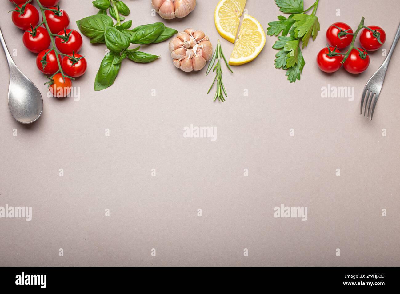 Komposition mit Zweig von frischen Kirschtomaten, Kräutern, Knoblauchzehen, Zitronenkeile, Küchenlöffel und Gabel auf minimalistischem grauen sauberen Hintergrund, V Stockfoto