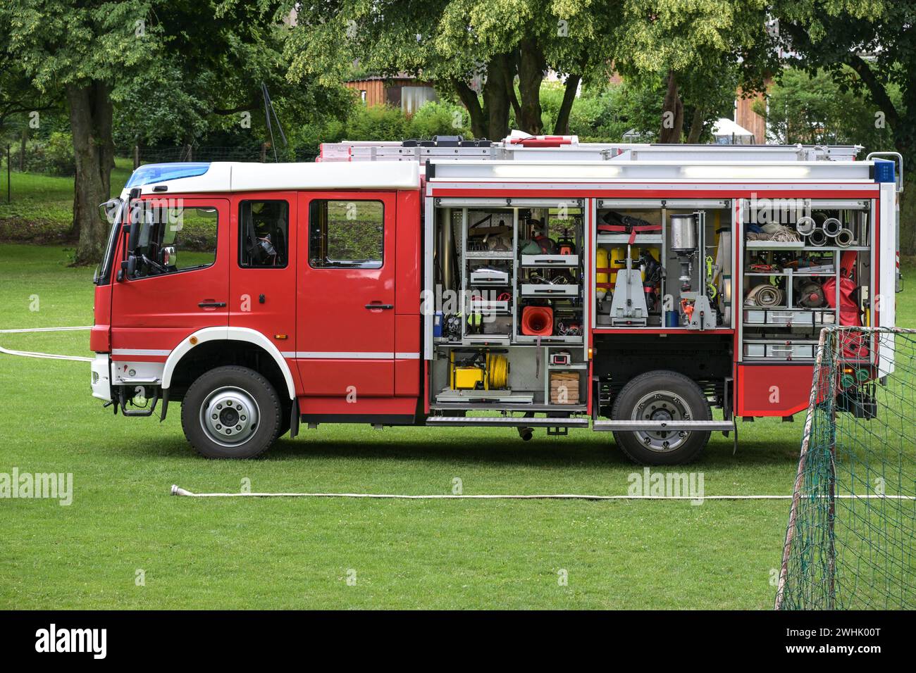 Deutsches Feuerwehrfahrzeug, roter Lkw mit offenen Rollladentüren und die Ausrüstung für Löscharbeiten, auf einer Wiese während einer Stockfoto