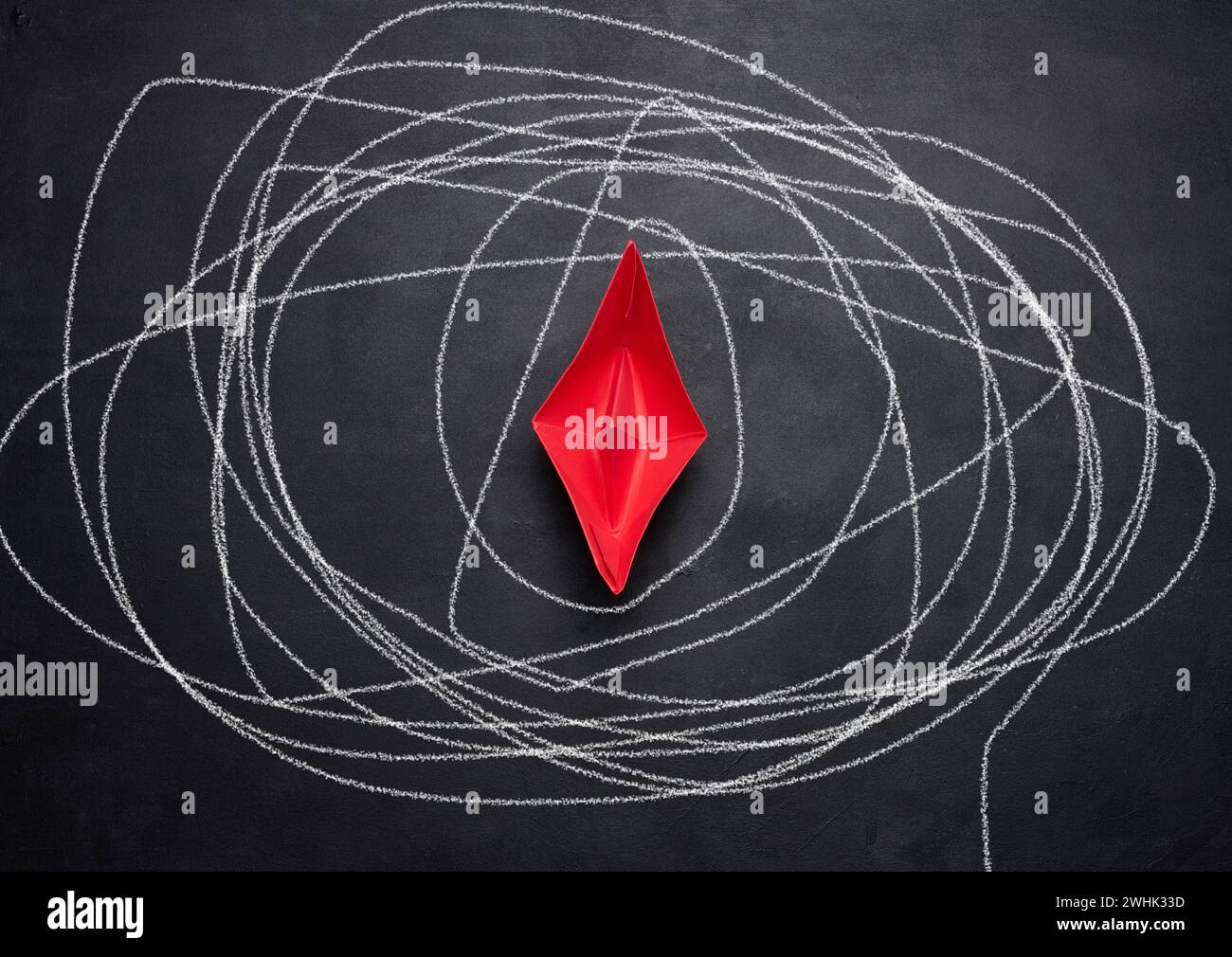 Rotes Papierboot auf schwarzer Tafel und ein langer, gezogener Pfad in weißer Kreide. Konzept einer schwierigen Reise, Suche nach Wahrheit Stockfoto