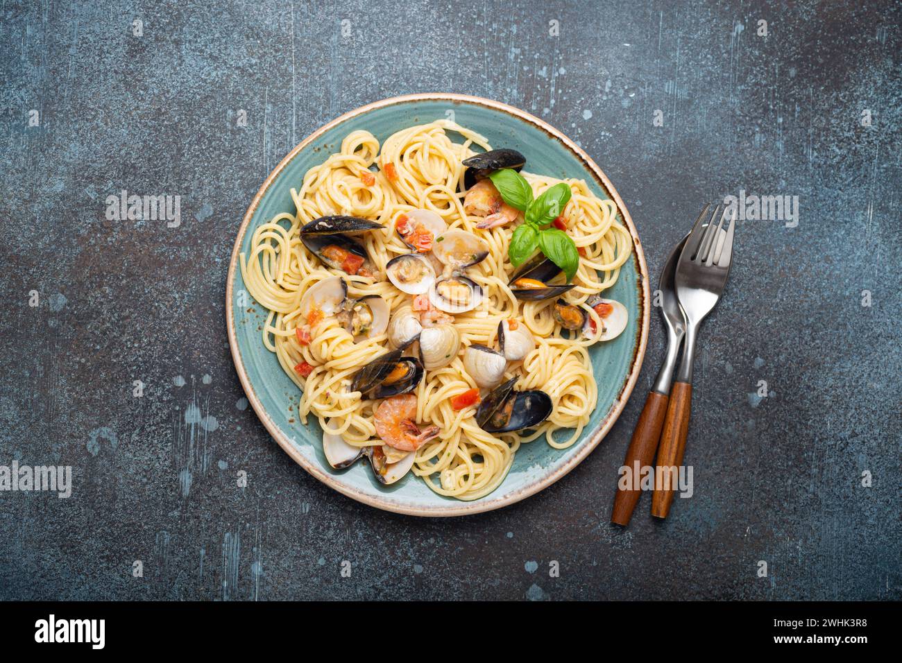 Spaghetti mit Meeresfrüchten, Muscheln, Garnelen, Muscheln in Tomatensauce mit grünem Basilikum auf Teller auf rustikalem blauem Beton b Stockfoto