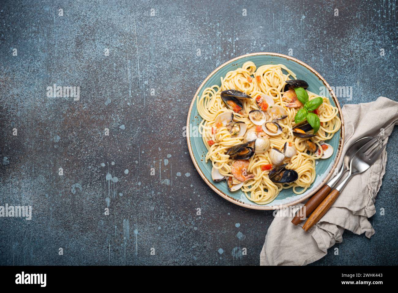 Spaghetti mit Meeresfrüchten, Muscheln, Garnelen, Muscheln in Tomatensauce mit grünem Basilikum auf Teller auf rustikalem blauem Beton b Stockfoto