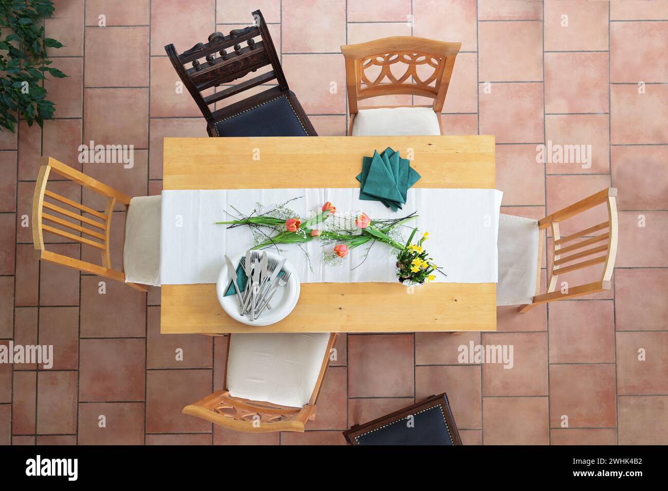Vorbereitung für eine Tischaufstellung mit weißen Tellern und Schüsseln, Besteck, grünen Servietten und einigen Tulpenblüten, verschiedenen Holzkaffee Stockfoto