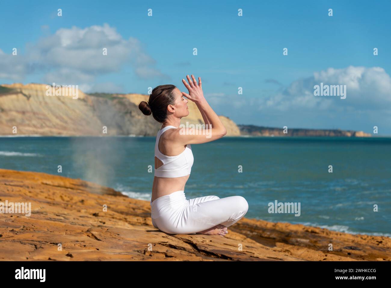 Sportliche Frau, die Yoga praktiziert und auf Felsen am Meer meditiert. Stockfoto