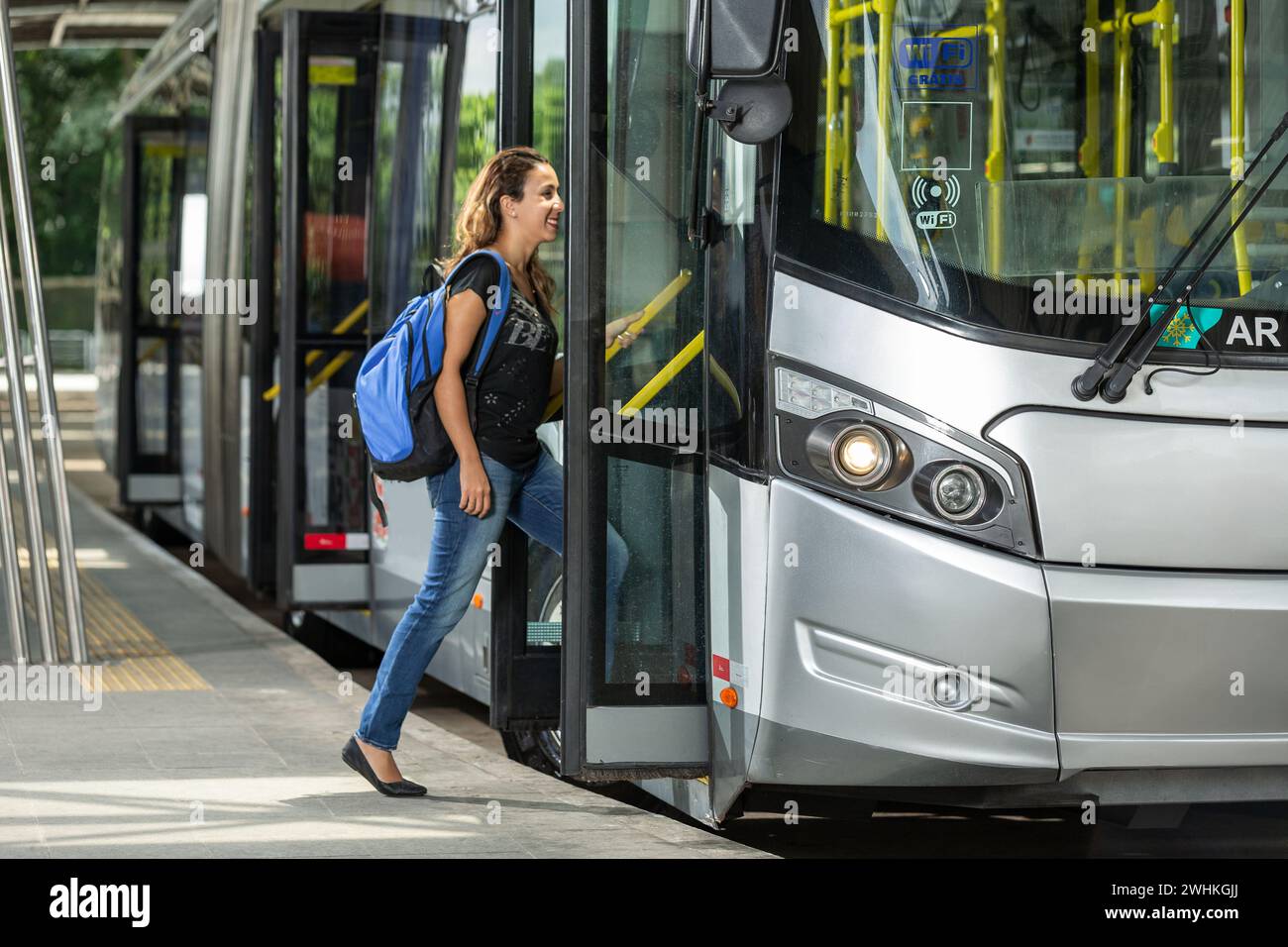 Ein Schüler mit Rucksack auf dem Rücken, der zur Schule ging, in einen modernen, grauen, zweigelenkigen Stadtbus stieg, hielt am Terminal Stockfoto