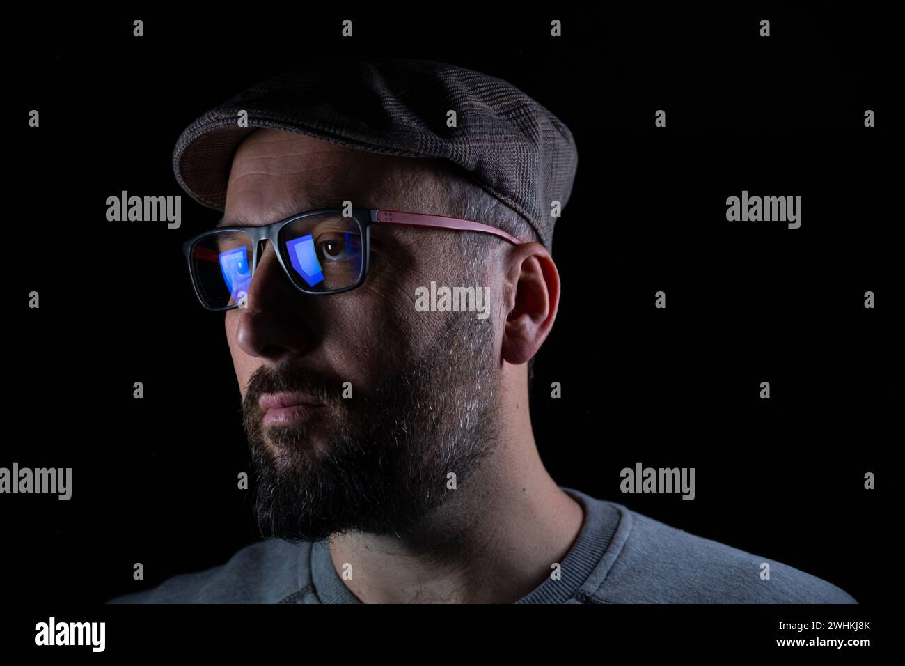 Dunkles Thema für Männer, die Brille und Mütze auf schwarzem Hintergrund mit ernstem Blick auf seinem Gesicht tragen Stockfoto