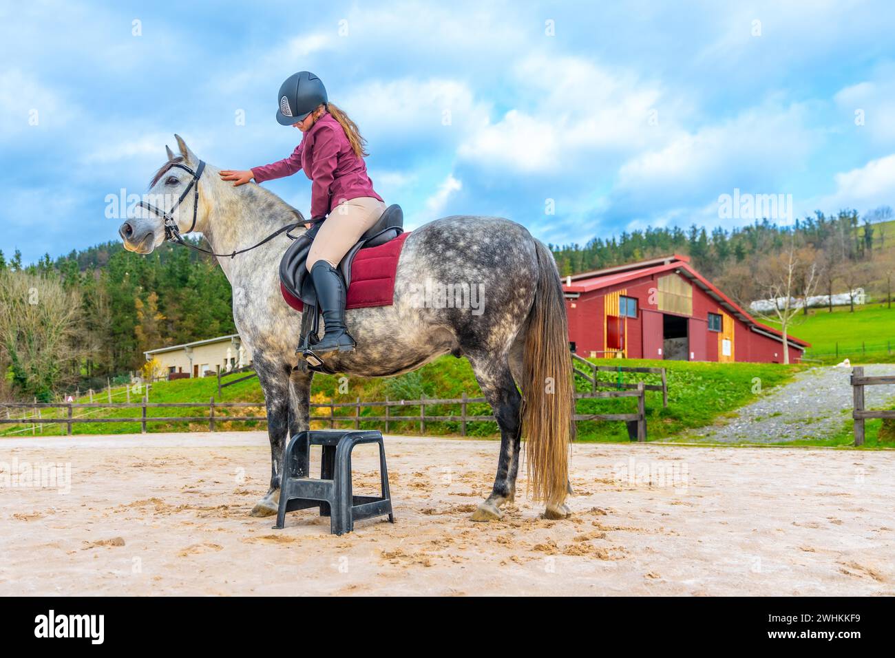 Mädchen mit Schutzausrüstung, das auf einem Pferd in einem Reitzentrum reitet Stockfoto