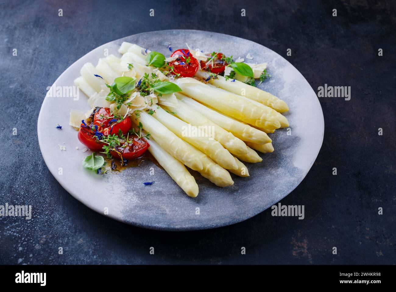 Weißer Spargel, glasiert mit Kirschtomaten und Parmesankäse, diente als Nahaufnahme auf einer Designplatte mit Textfeld Stockfoto