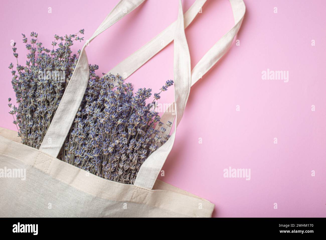 Lavendelblumen Blumenstrauß in beige Öko-Leinen Einkaufstasche auf lila Hintergrund von oben View. Romantischer Frühling oder Sommer mädchenhaft feminin Stockfoto