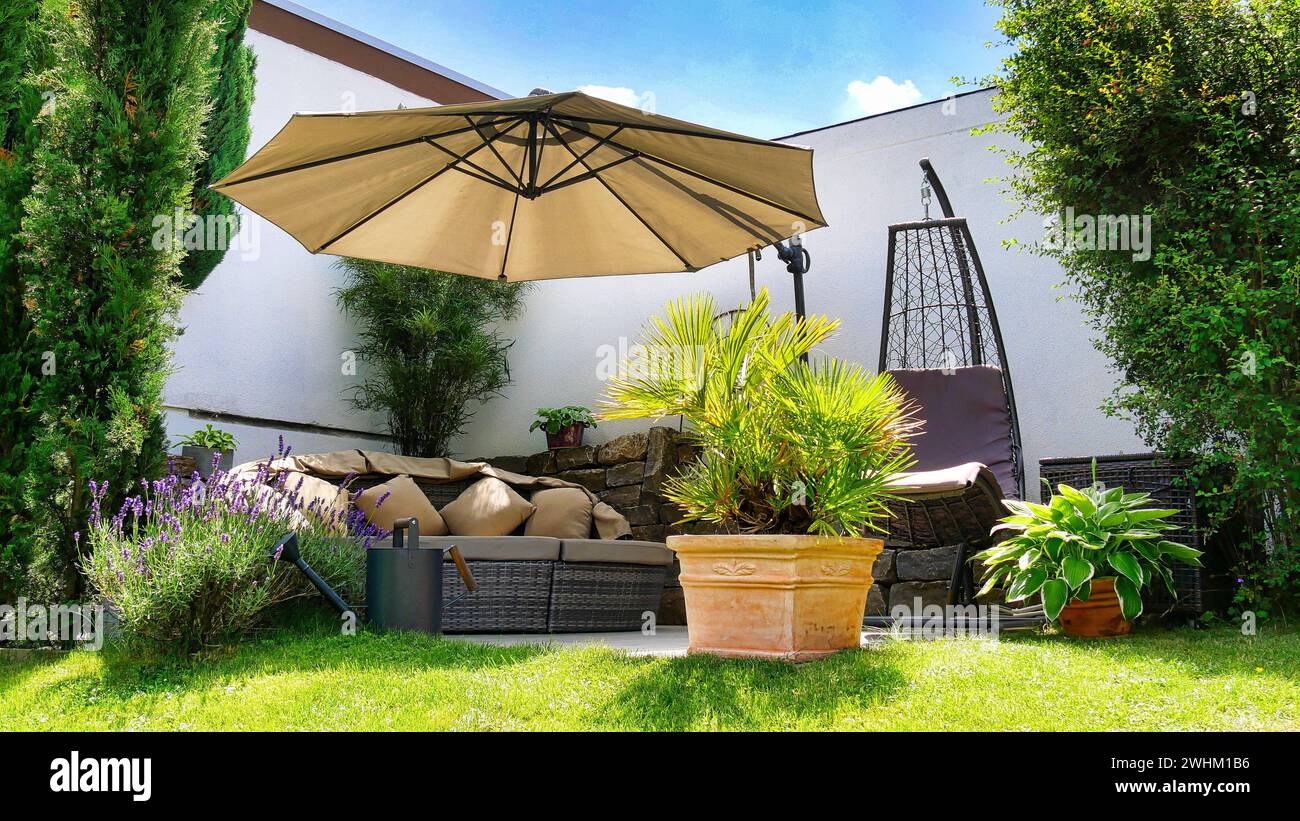 Gartenterrasse mit Loungegruppe und Sonnenschirm in einer Gartenecke mit verschiedenen Pflanzen Stockfoto