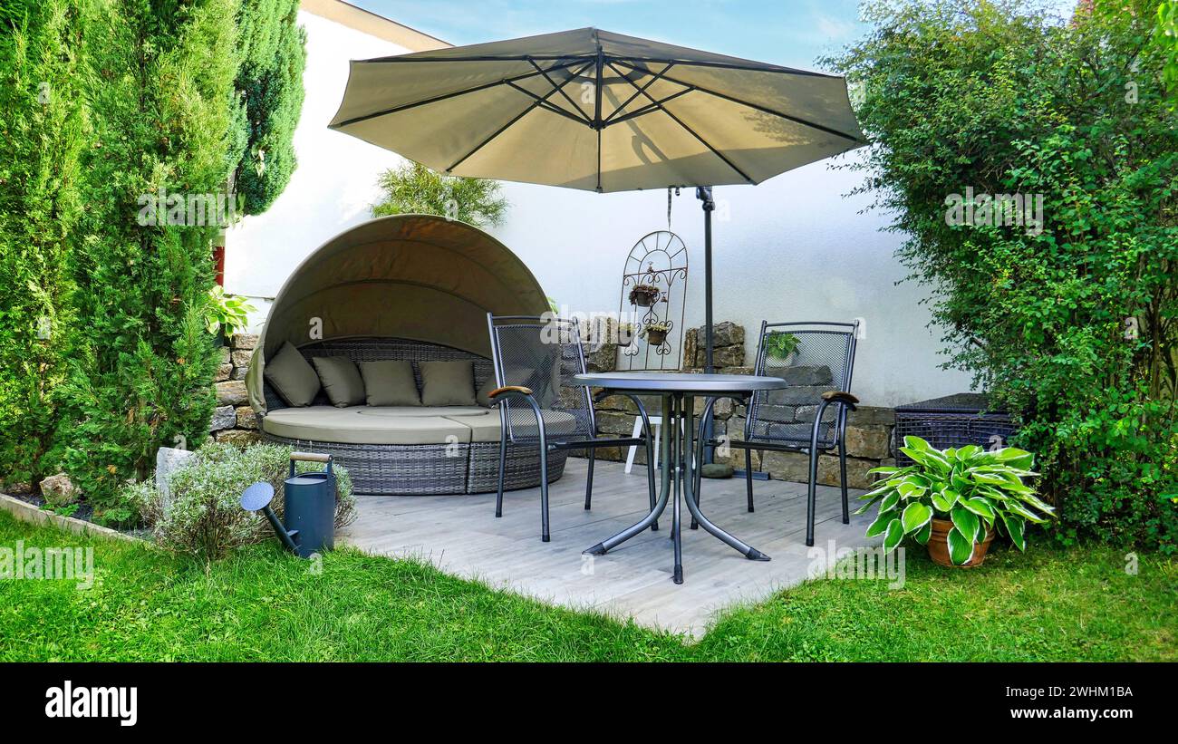 Gartenterrasse mit Lounge und Sitzbereich und Sonnenschirm in einer Gartenecke mit verschiedenen Pflanzen Stockfoto