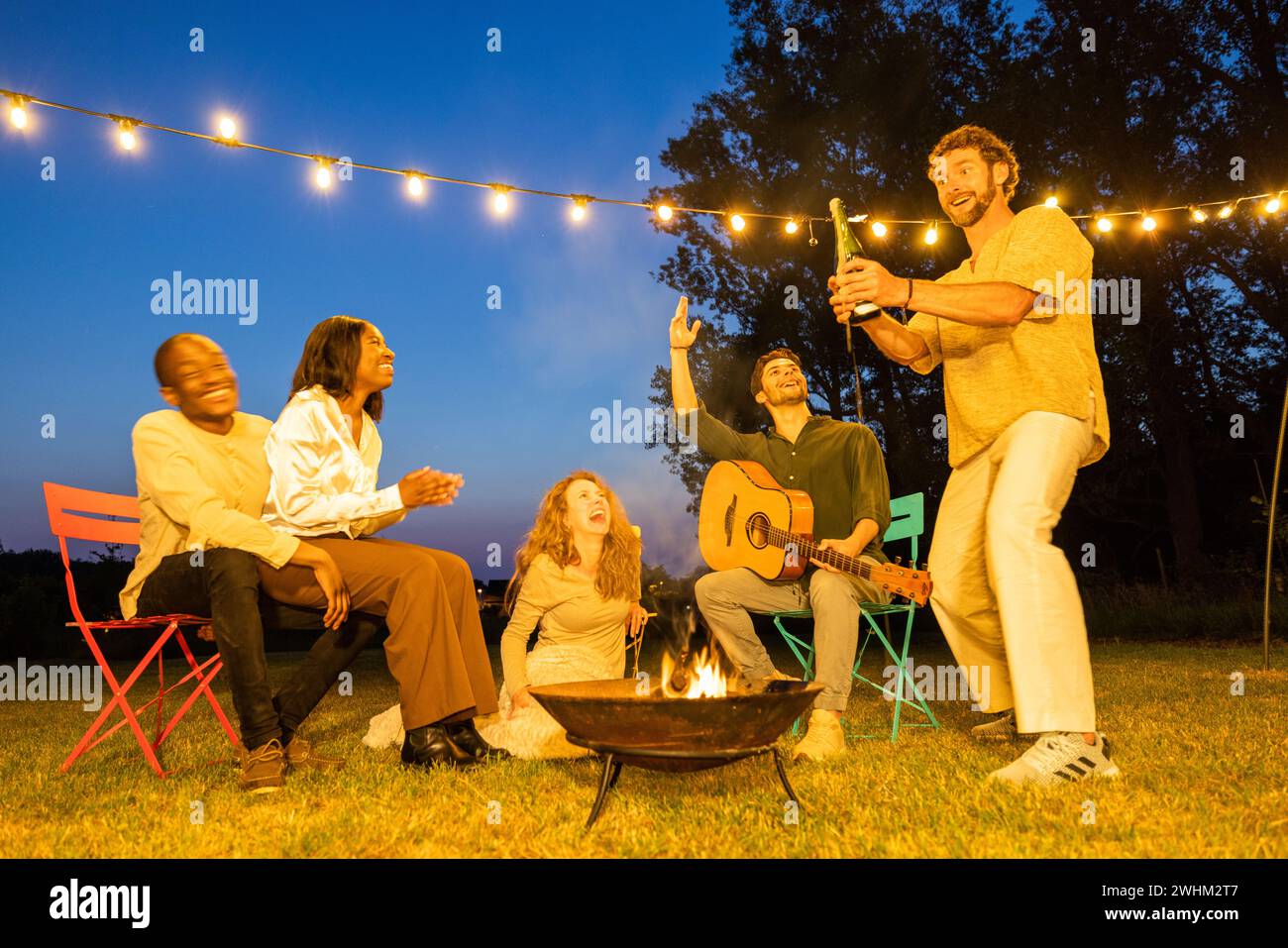 Lebendige Gartenparty: Freunde vereinigen sich mit Musik und Lachen, einer multiethnischen Gruppe von Freunden auf einer Gartenparty am Abend ha Stockfoto