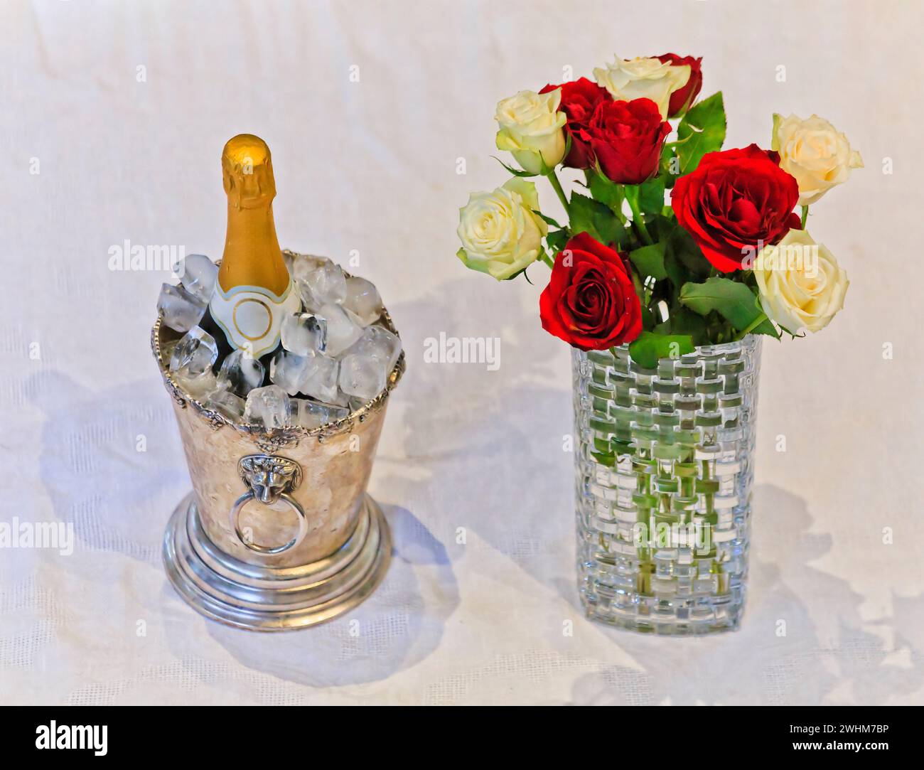 Luxuriöser Lebensstil mit einer Flasche Weißwein im Eiskübel und Blumenstrauß in einer Vase auf weißem Tischtuch. Stockfoto