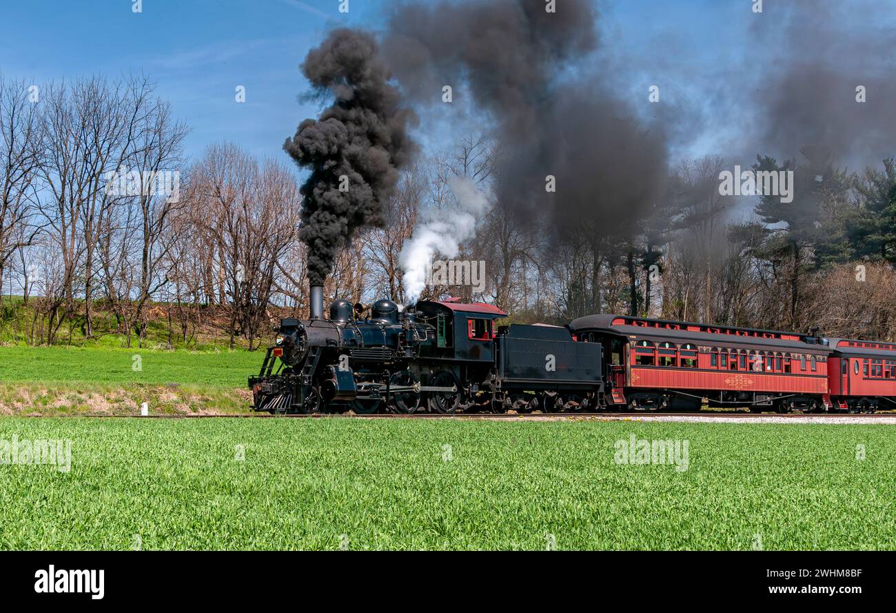 Abgewinkelter Blick auf einen restaurierten Dampfzug, der langsam viel schwarzen Rauch bläst Stockfoto