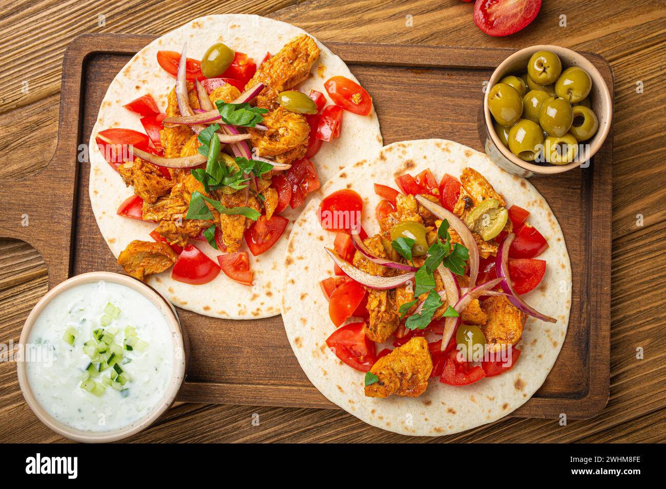 Traditionelles griechisches Gericht Gyros: Pita-Brot mit Gemüse, Fleisch, Kräutern, Oliven auf rustikalem Holzschneidebrett mit Tzatzi Stockfoto