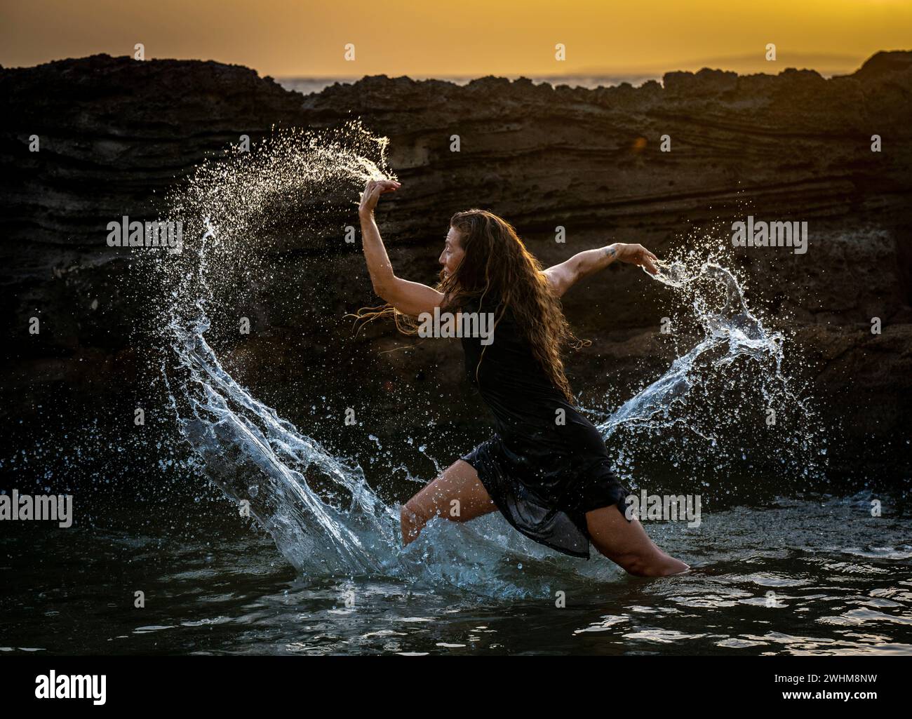 Eine Frau mittleren Alters, die tanzt und Wasser in die Luft wirft Stockfoto