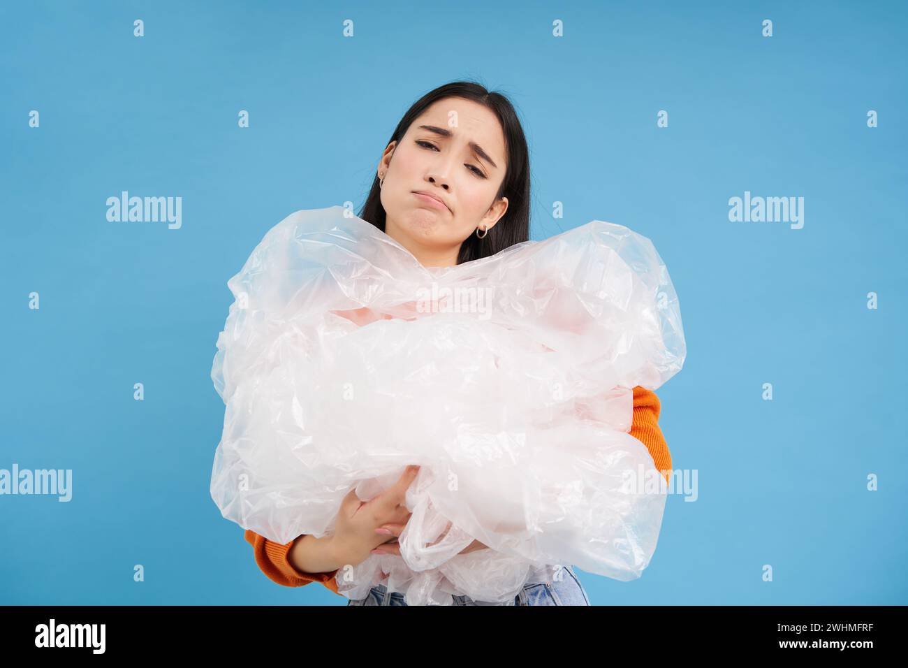 Asiatische traurige Frau mit Plastikmüll und Stirnrunzeln vor Enttäuschung, Kampf gegen Verschmutzung, Öko-Aktivist sortiert Abfall, blauer Ba Stockfoto