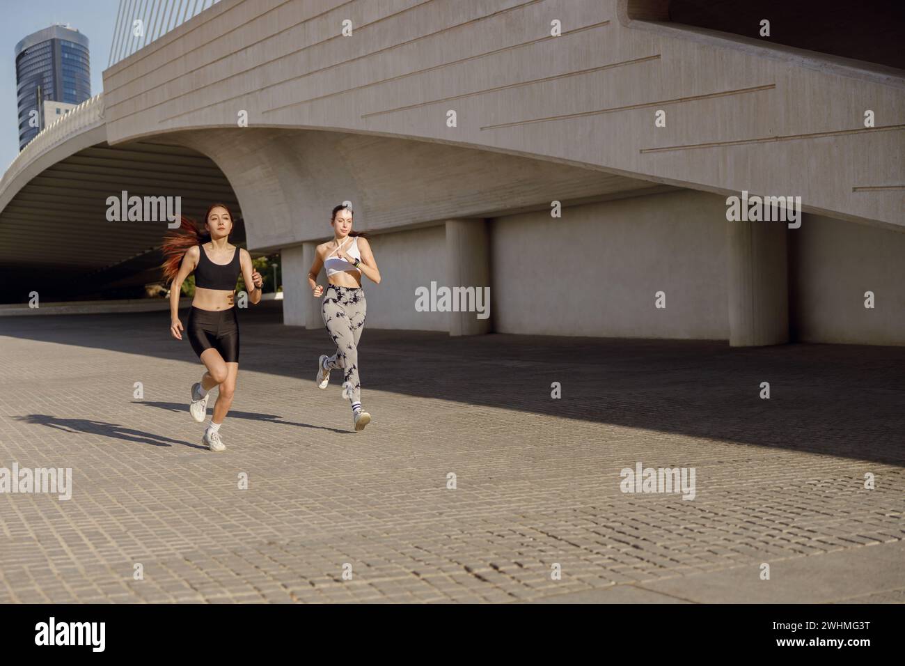 Zwei aktive Athleten laufen Seite an Seite auf einer Outdoor-Strecke auf modernem Gebäudehintergrund Stockfoto