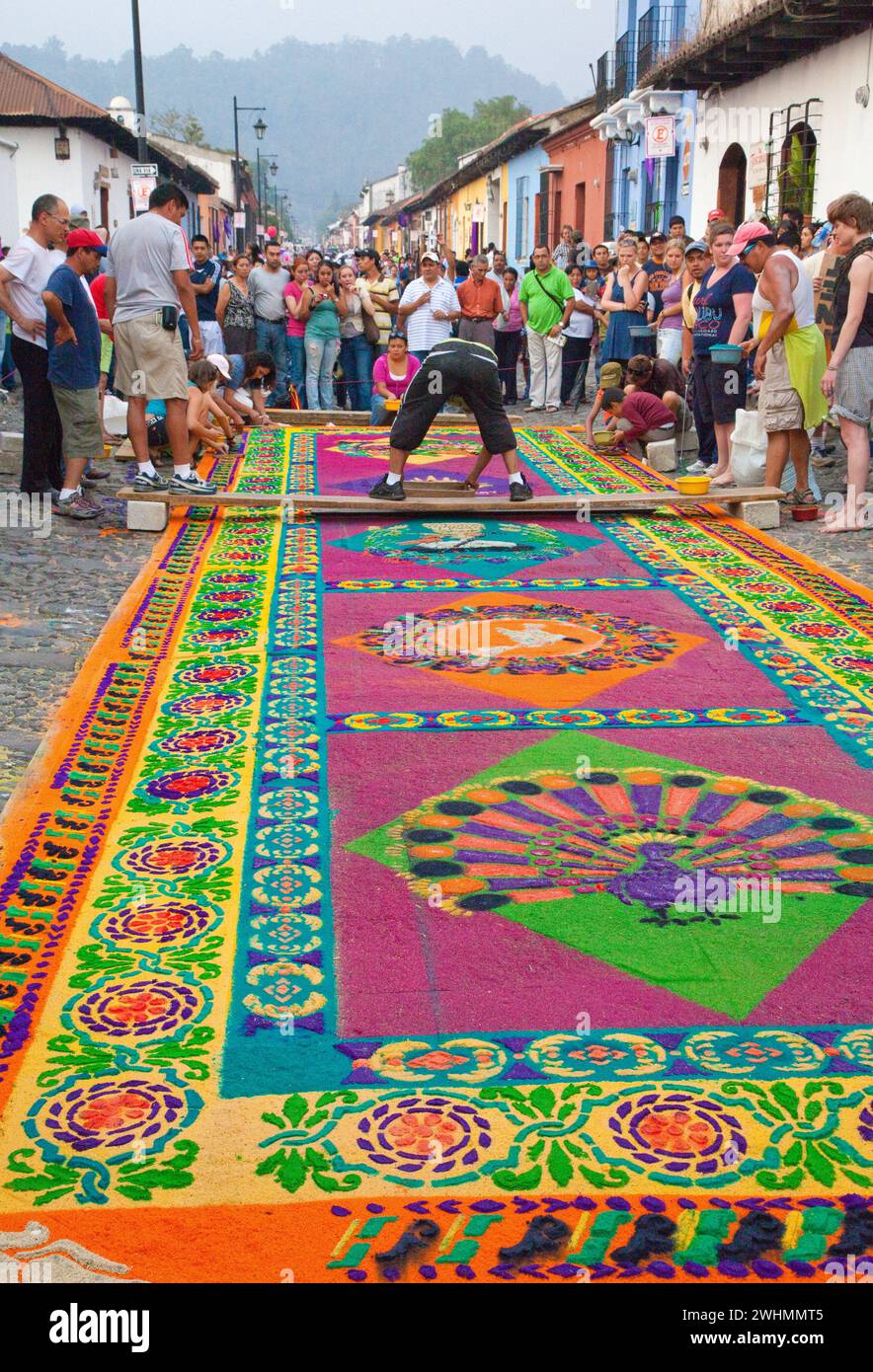 Antigua, Guatemala. Semana Santa, Karwoche. Die Zuschauer beobachten, wie Künstler einen Alfombra (Teppich) aus farbigem Sägemehl zum Dekorieren veredeln Stockfoto