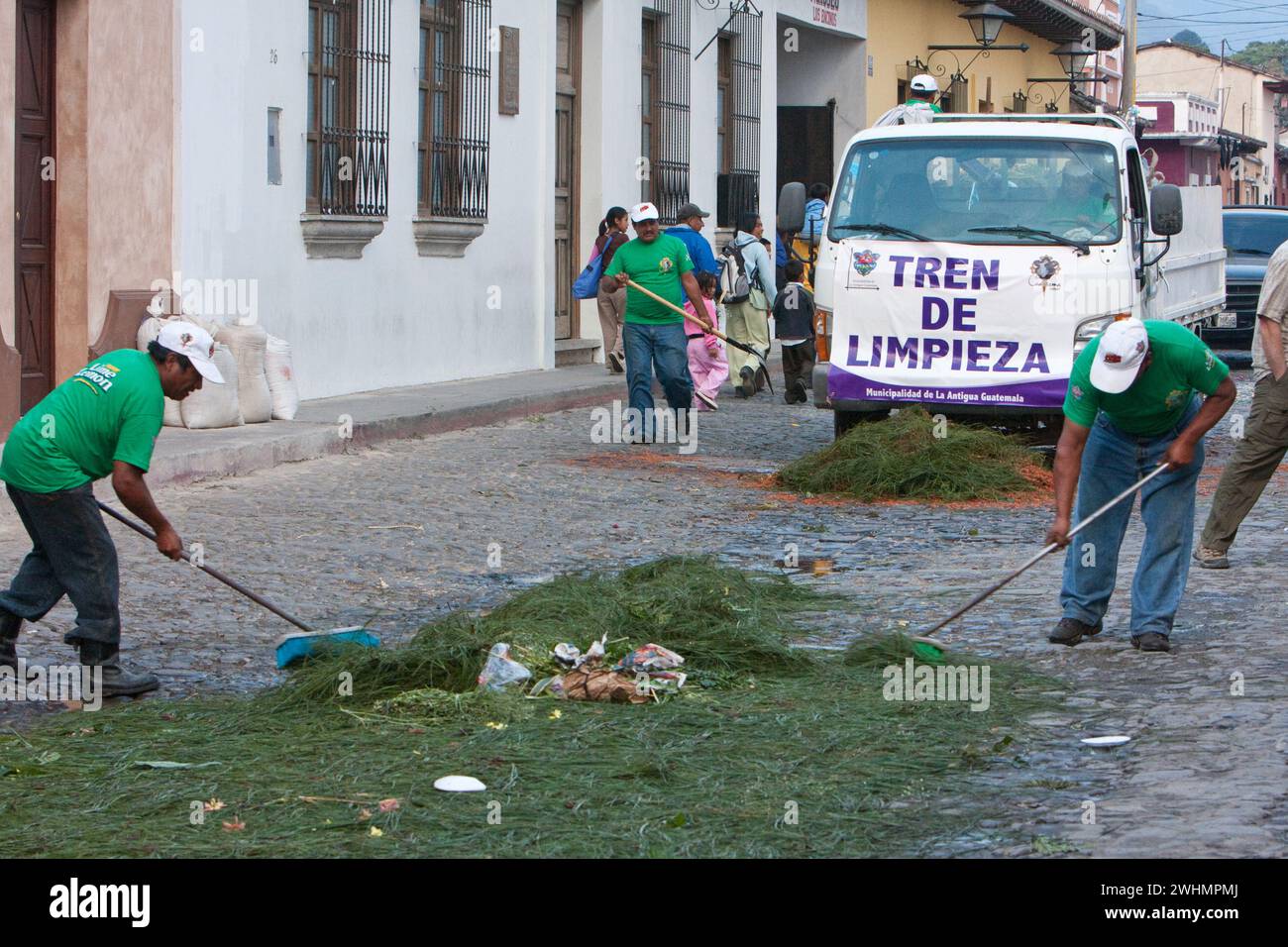 Antigua, Guatemala. Die Straßenreinigung fegt die Überreste eines Alfombra (Teppichs) aus Blumen, Kiefernnadeln und anderen traditionellen Materialien sofort auf Stockfoto