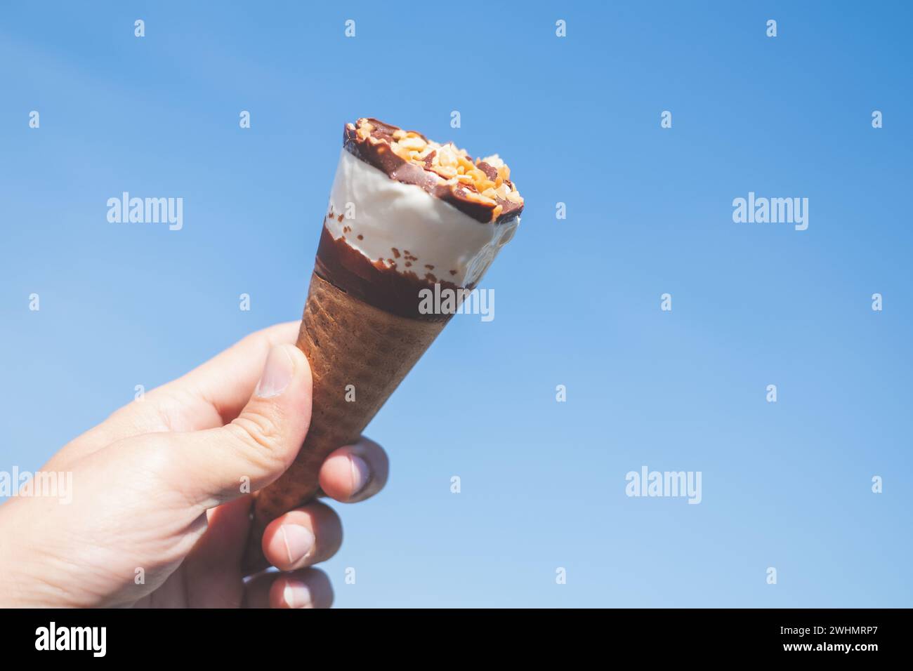 Hand hält einen Eiskegel mit blauem Himmel Hintergrund Stockfoto