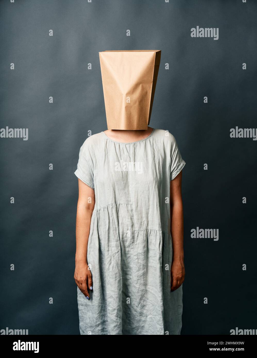 Frau im Kleid mit einer Papiertüte auf dem Kopf, die über dunklem Hintergrund steht Stockfoto