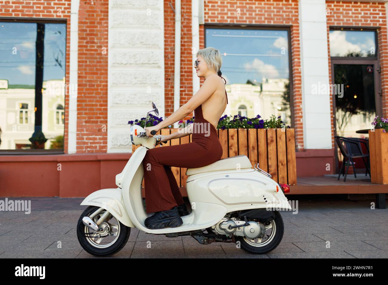 Junge Frau, die auf einem Motorrad-Moped-Roller in der Stadtstraße fährt. Stockfoto