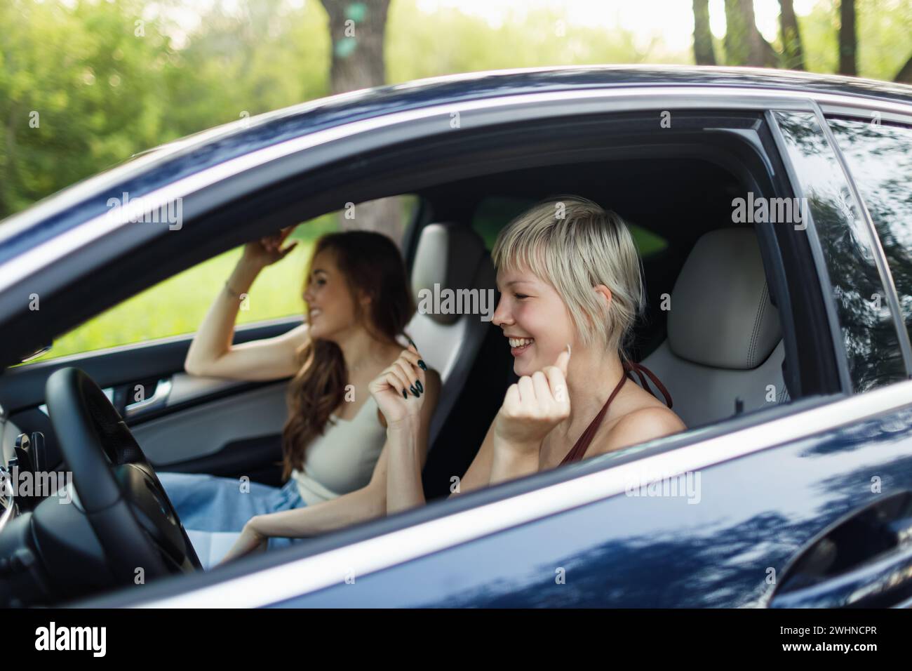 Zwei Fahrerinnen im Auto lächelnd und tanzen hans auf. Süße junge glückliche Frau, die Auto fährt. Stockfoto