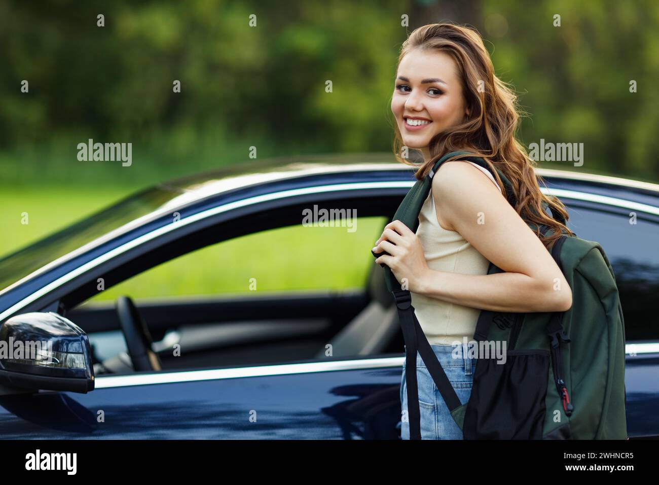 Glückliche Fahrerin bekommt Auto mit Rucksack. Süße junge glückliche brünette Frau, die Auto fährt. Stockfoto