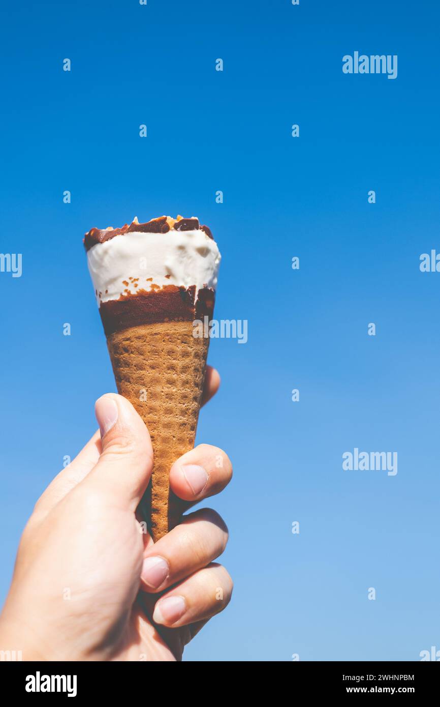 Hand hält einen Eiskegel mit blauem Himmel Hintergrund Stockfoto