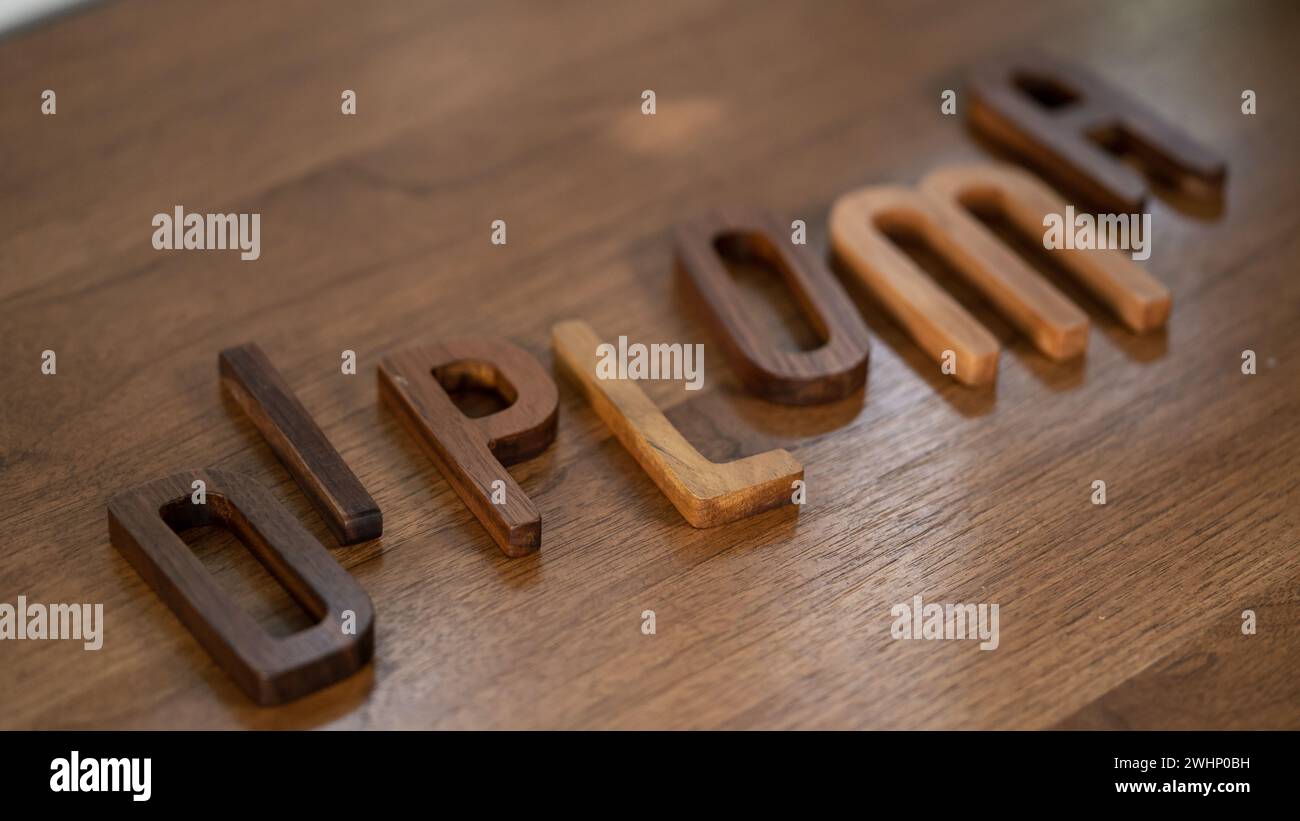 Handwerkliche Einrichtung: 3D-Briefe mit „Diplom“-Schriftzug aus Nussbaum zieren den Holztisch Stockfoto