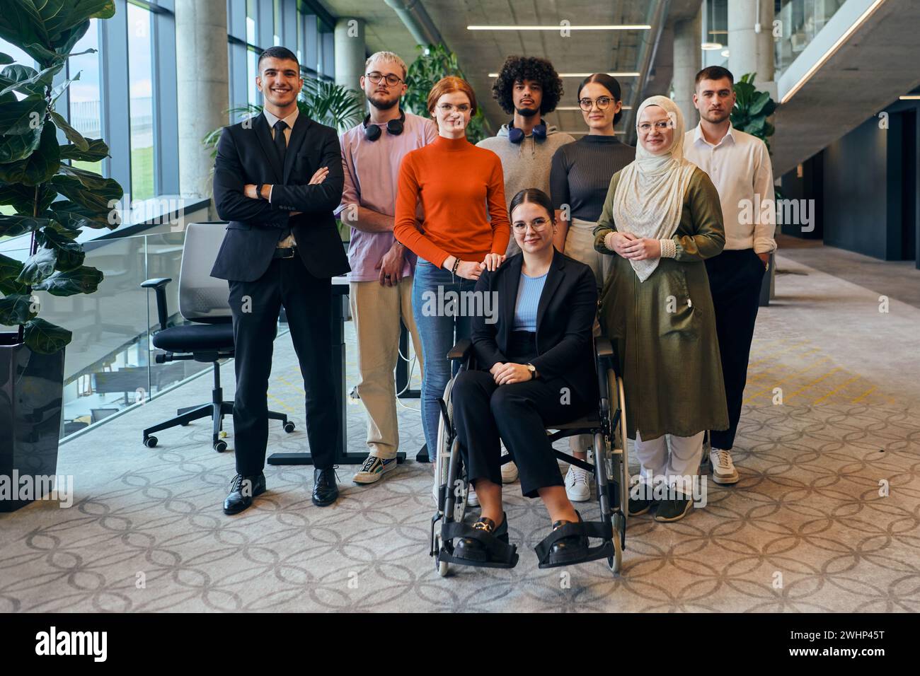 In einem geräumigen und modernen Startup-Büro gibt es eine Gruppe von Geschäftskollegen, darunter ein Kollege im Rollstuhl, Kollabor Stockfoto