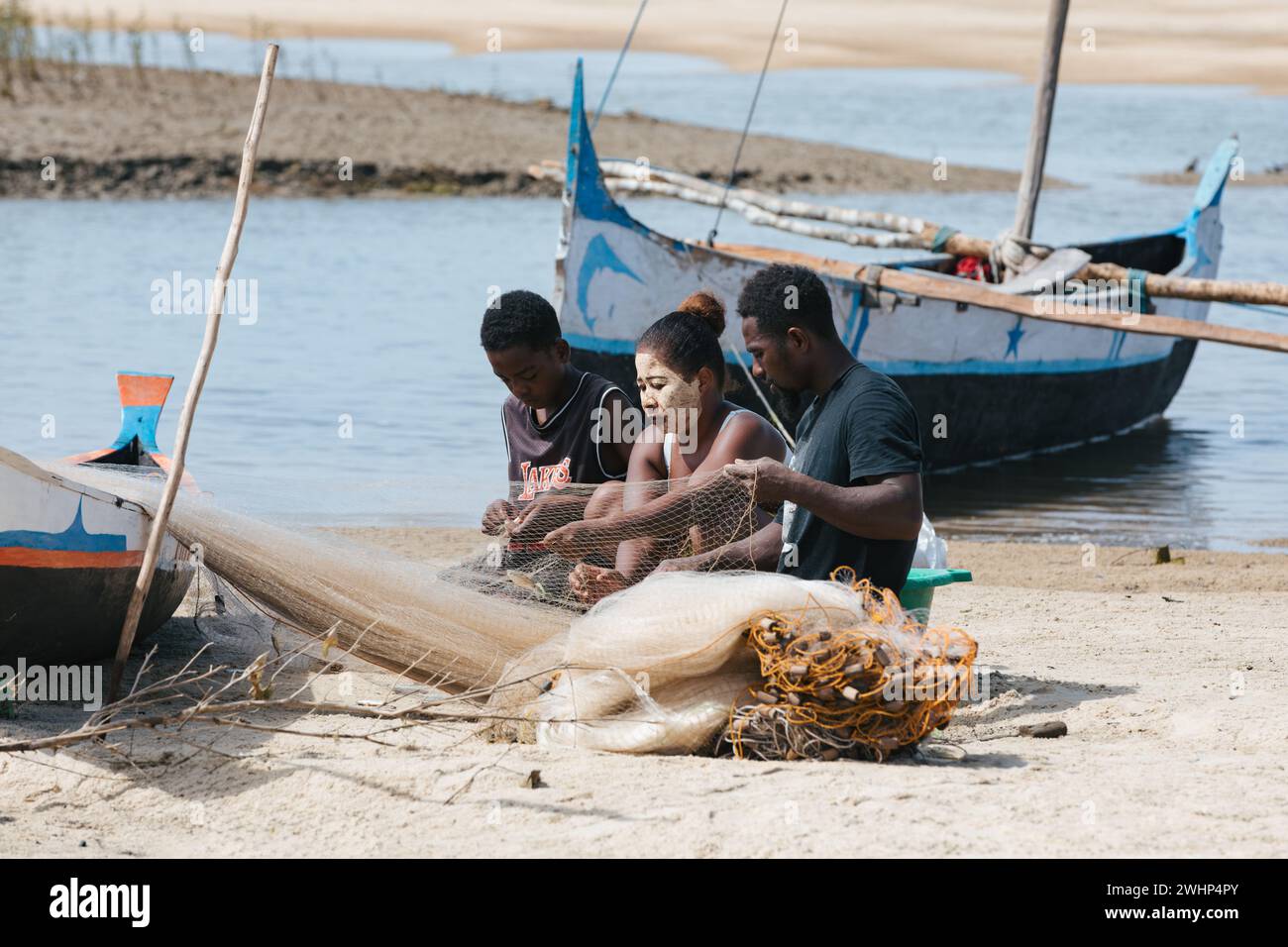 Fischer und Frauen reparieren Fischernetze an den Flussmündungen. Die Frau hat ein traditionell madagassisches Gesicht Stockfoto