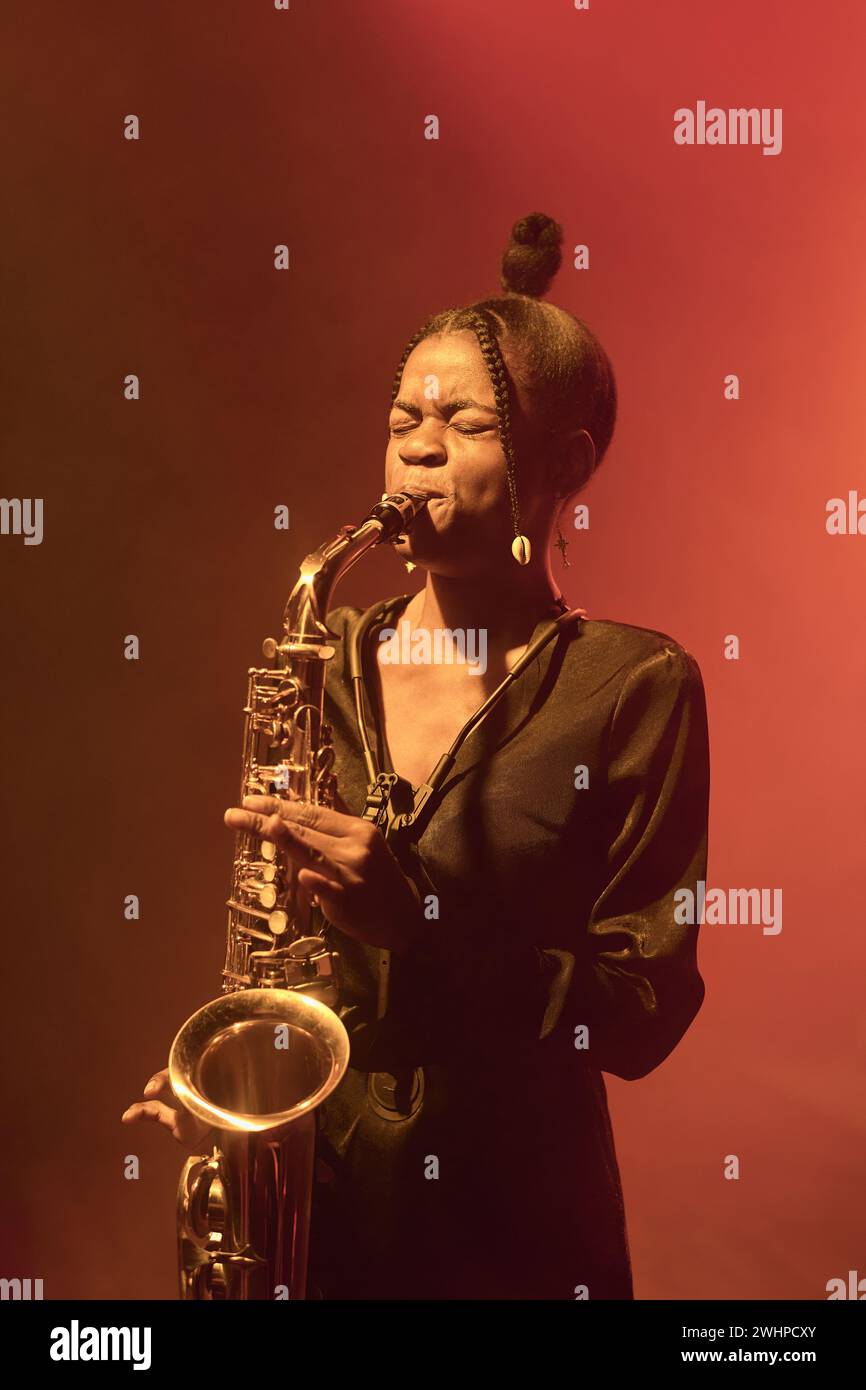 Vertikales Porträt einer afroamerikanischen jungen Frau, die Saxophon spielt, während sie Jazzmusik auf der Bühne im Club aufführt Stockfoto