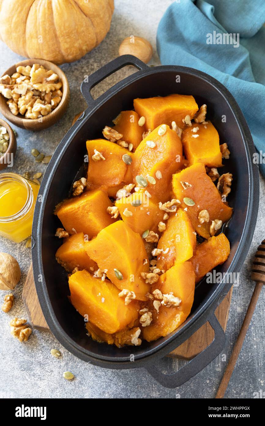 Gesundes Dessert oder veganes Mittagessen. Gebackener Kürbis. Köstlicher gebackener süßer Kürbis mit Nüssen, Kürbiskernen und Honig über grauem Stein Stockfoto