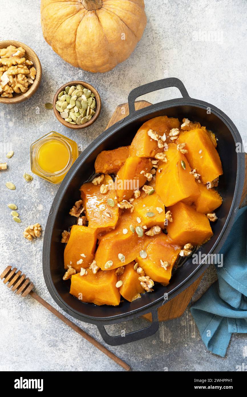 Gesundes Dessert oder veganes Mittagessen. Gebackener Kürbis. Köstlicher gebackener süßer Kürbis mit Nüssen, Kürbiskernen und Honig über grauem Stein Stockfoto