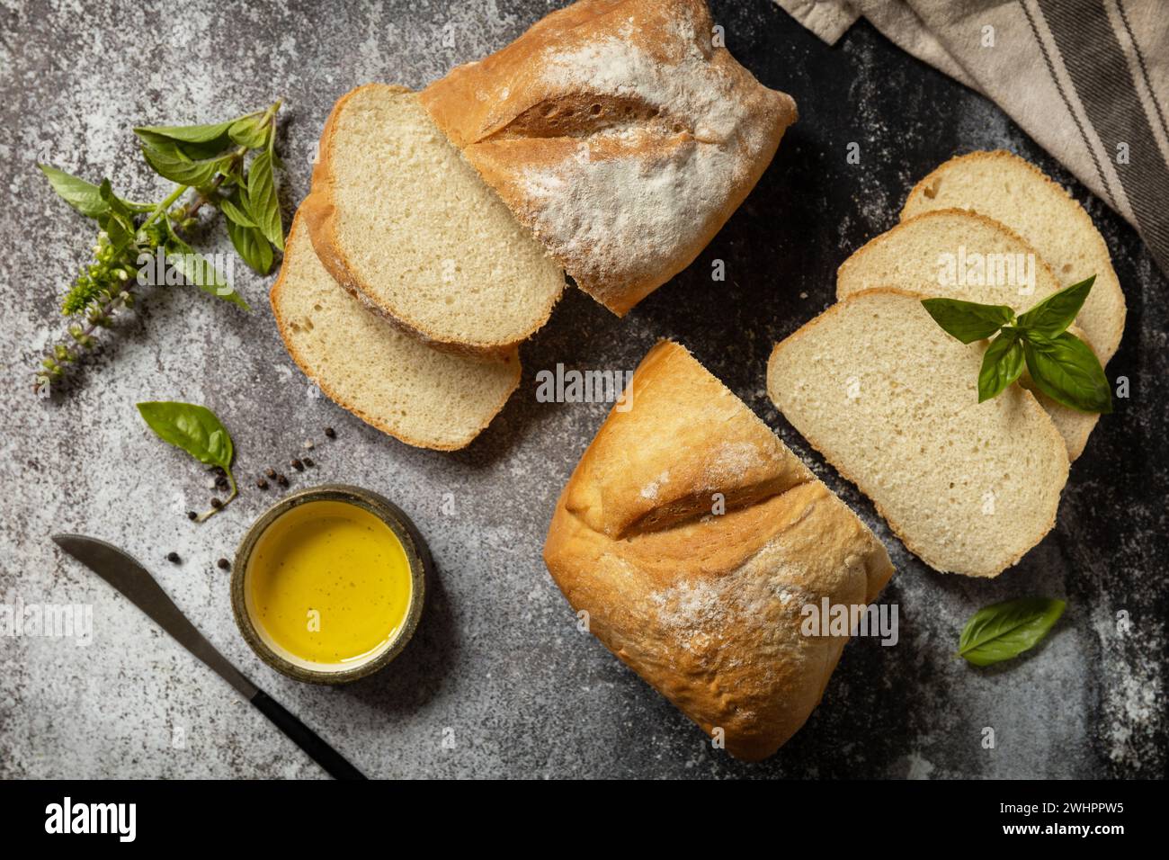 Geschnittenes italienisches Ciabatta-Brot mit extra nativem Olivenöl und Kräuter auf dunklem Steinhintergrund. Frisches, knuspriges Ciabatta-Brot. Ansicht Stockfoto