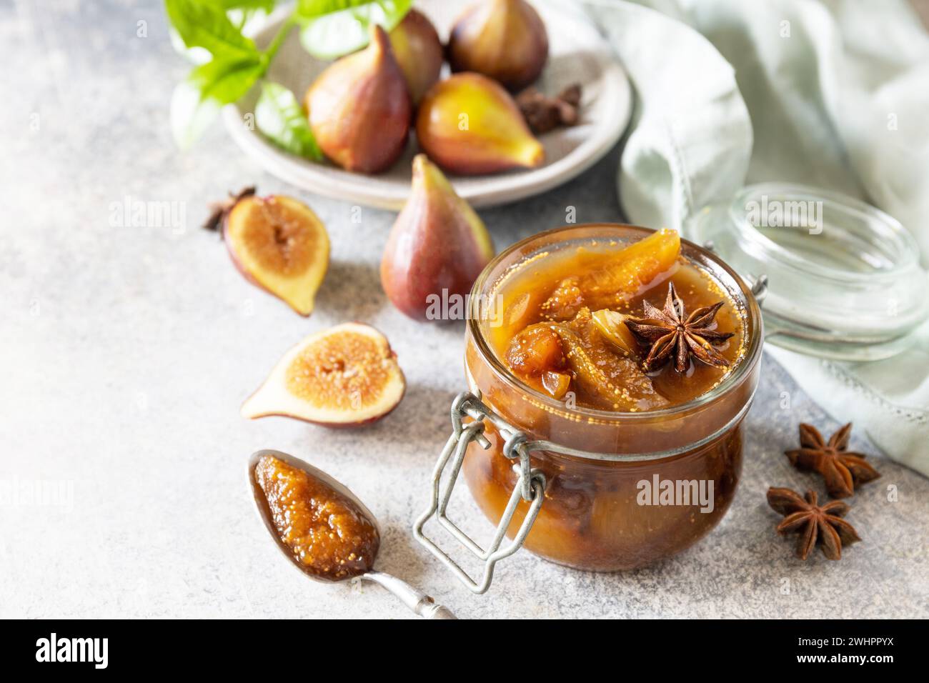 Hausgemachte süße Feigen-Marmelade in einem Glasgefäß mit frischen Feigen auf einem hellgrauen Tisch. Herbsternterhaltung, gesunde fermentierte Nahrung Stockfoto