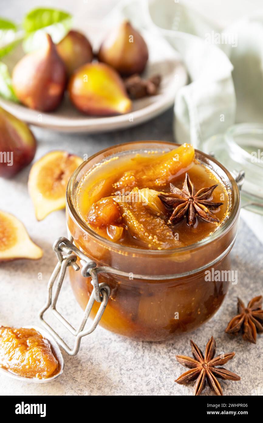 Hausgemachte süße Feigen-Marmelade in einem Glasgefäß mit frischen Feigen auf einem hellgrauen Tisch. Herbsternterhaltung, gesunde fermentierte Nahrung Stockfoto