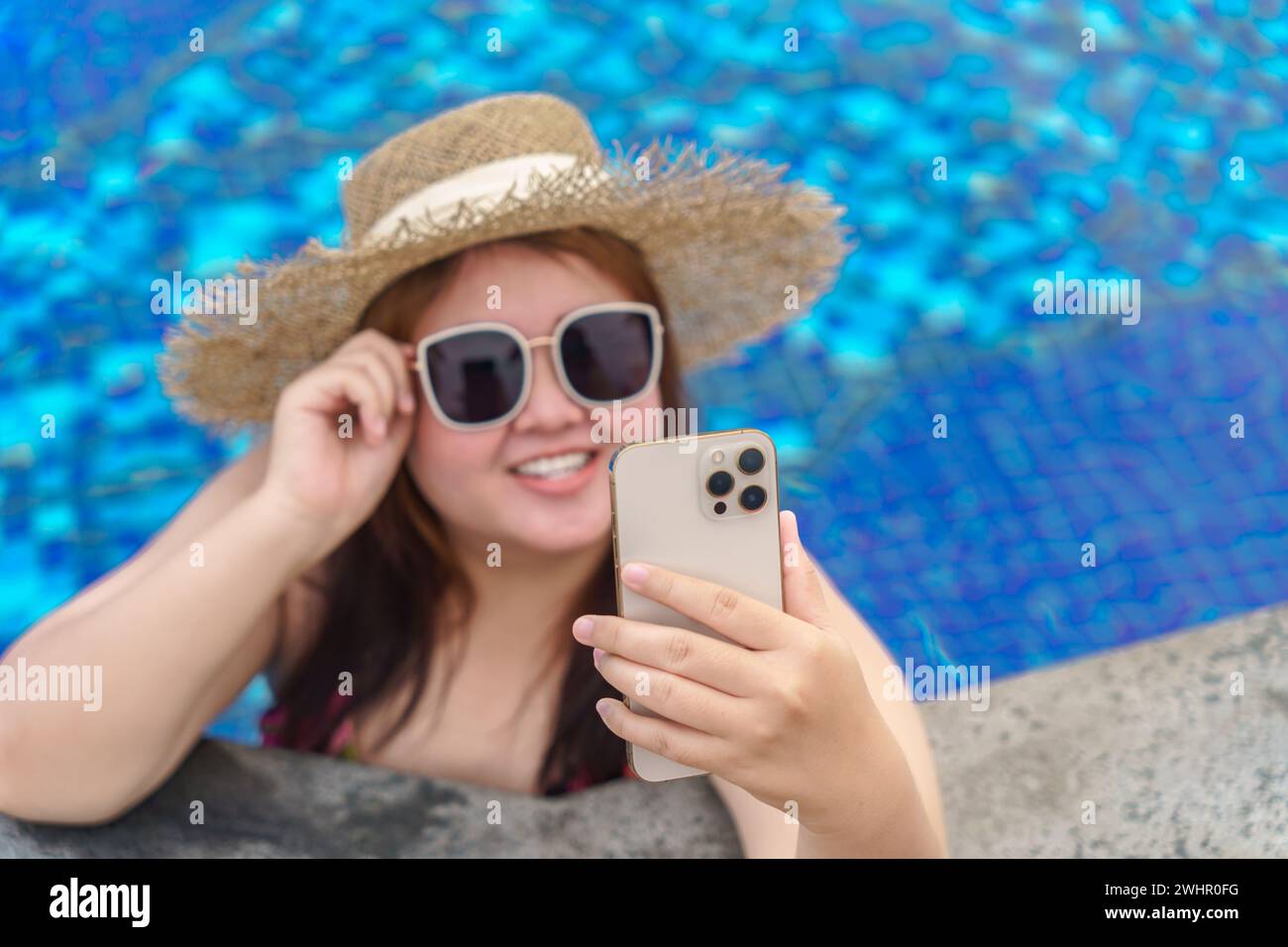 Übergewichtige junge Frau orange swimsuitÂ entspannt und hält Smartphone im Schwimmbad. Fettleibige Frau Urlaub Reisender Hand uns Stockfoto
