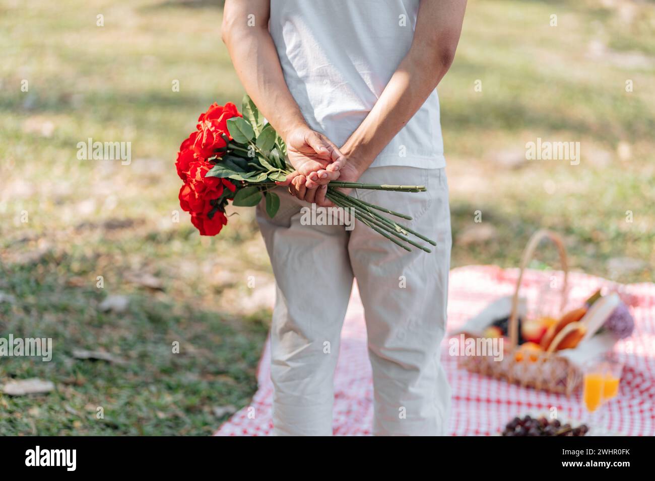 Glückliches romantisches Paar am Valentinstag asiatischer Mann, der rote Rosenblume hinter sich versteckt, um seine Freundin zu überraschen. Stockfoto