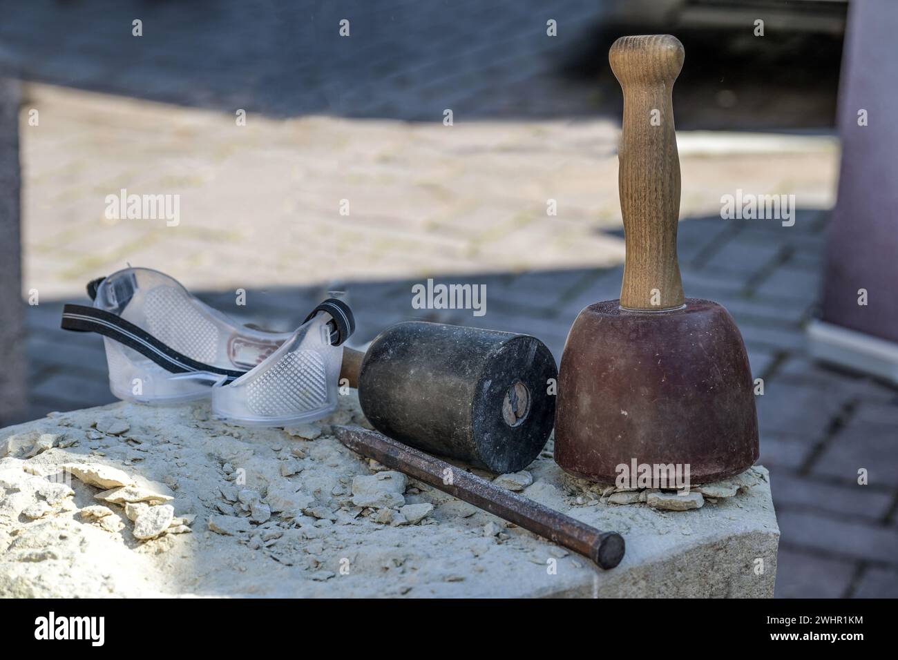 Werkzeuge aus einem Steinmetzwerk, bestehend aus kunststoffbeschichteten Holzhämmern, Meißel und Schutzbrille auf einem grauen Stein, traditionelle cra Stockfoto